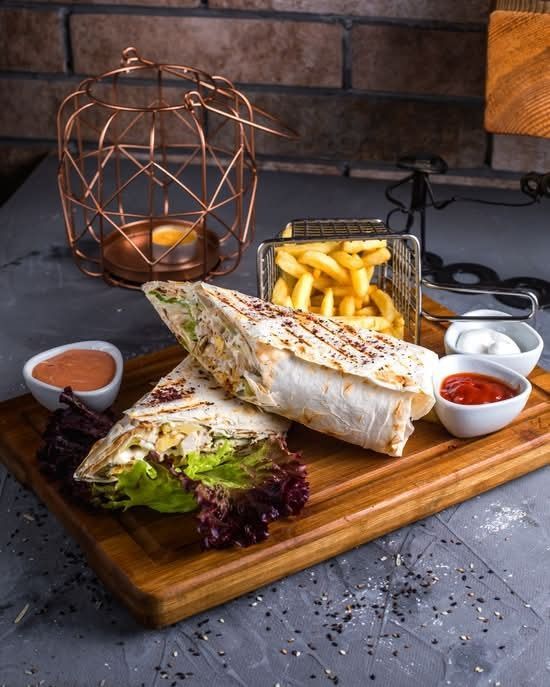 Wrap a la parrilla con patatas fritas y salsas para mojar sobre una tabla de madera en un ambiente de cocina rústica.