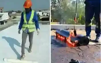 Uma pessoa utiliza um maçarico para instalar material de cobertura em um telhado plano. Um rolo de material é visível.