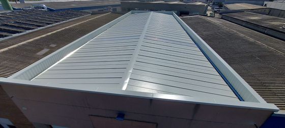 Vista desde un ángulo elevado de un tejado plano de color gris claro con una textura estampada prominente, rodeado de superficies de tejado más oscuras y acanaladas.