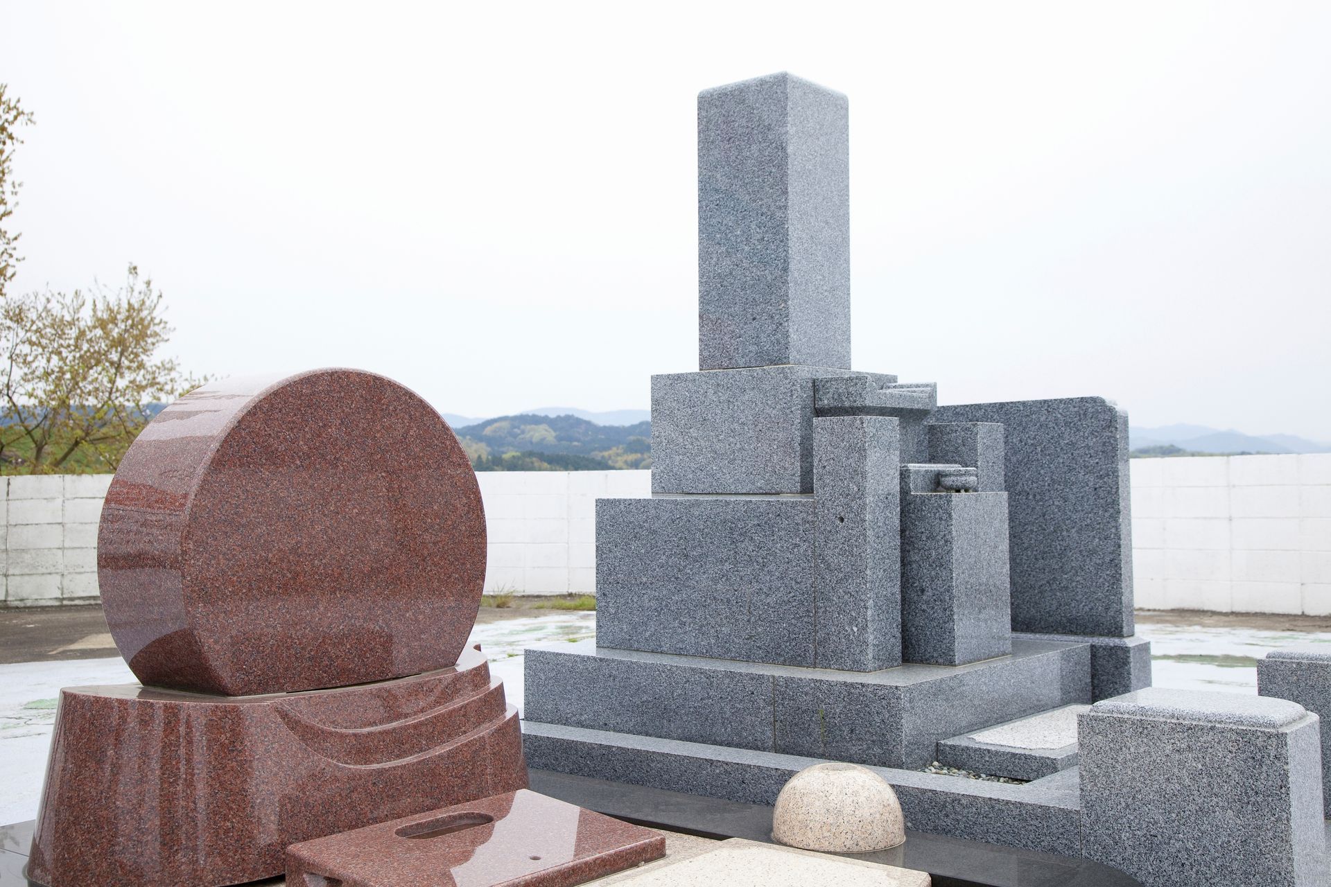Des pierres tombales en granit de formes et de couleurs variées se détachent sur un ciel nuageux.
