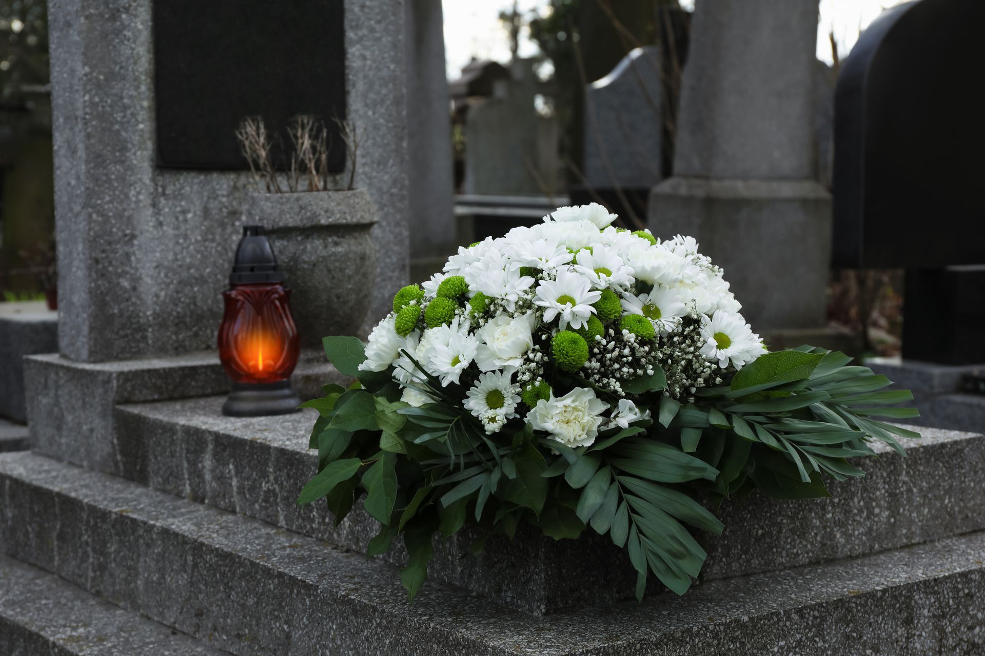 Des fleurs blanches et une bougie sur une pierre tombale grise dans un cimetière.