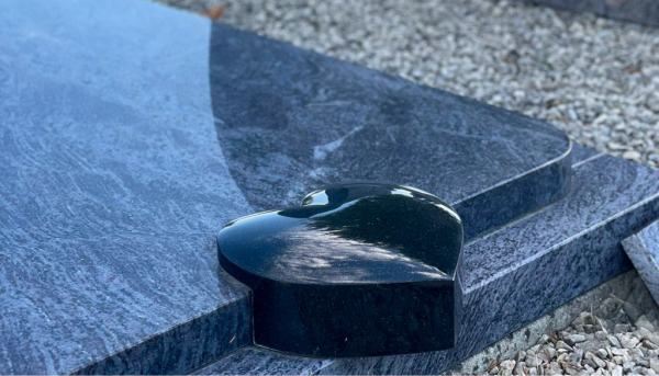 Gros plan sur une pierre tombale en granit noir, de forme incurvée et ornée d'un détail poli en forme de cœur.