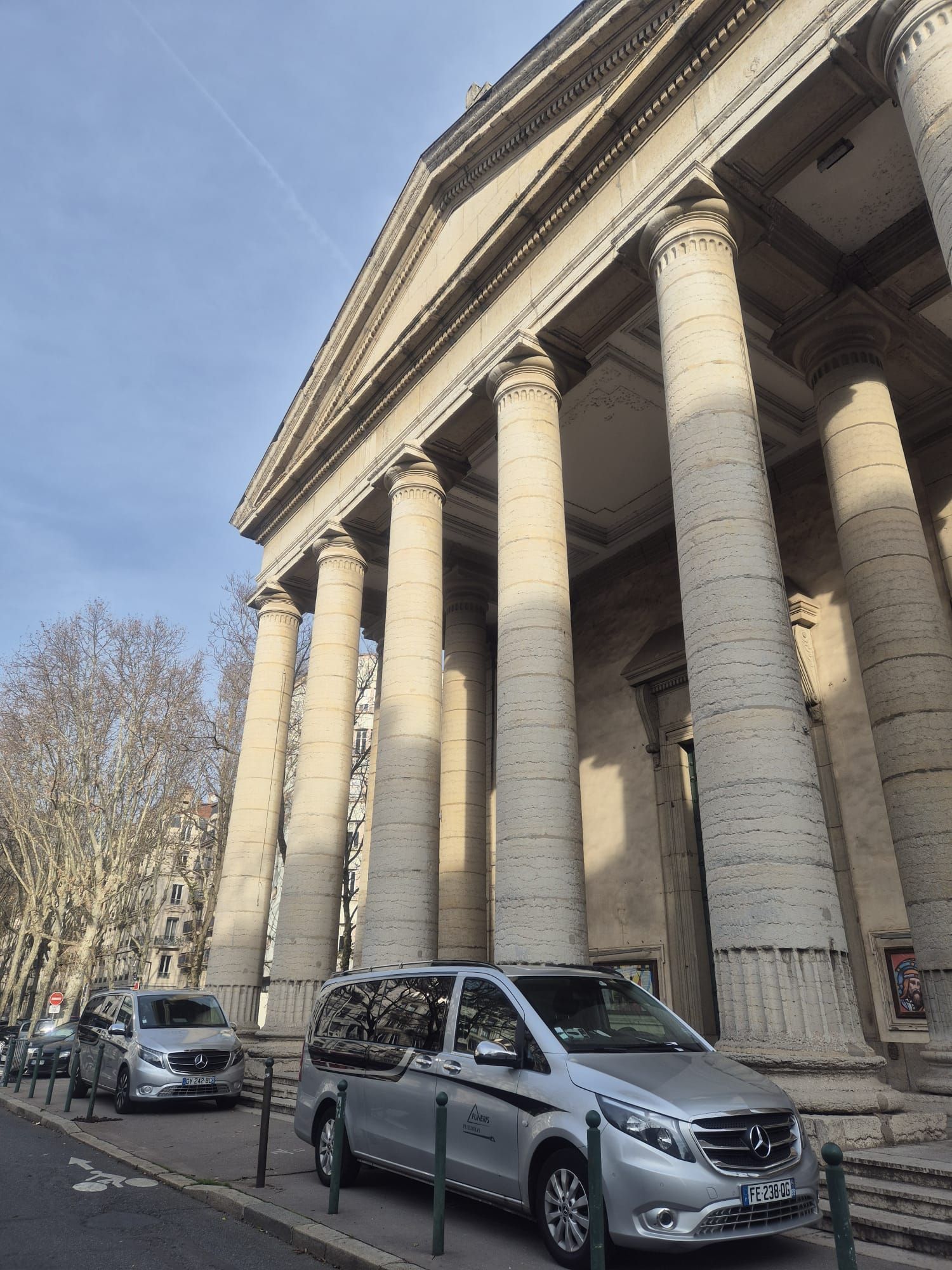 Immeuble aux hautes colonnes ; camionnettes argentées garées dans la rue.
