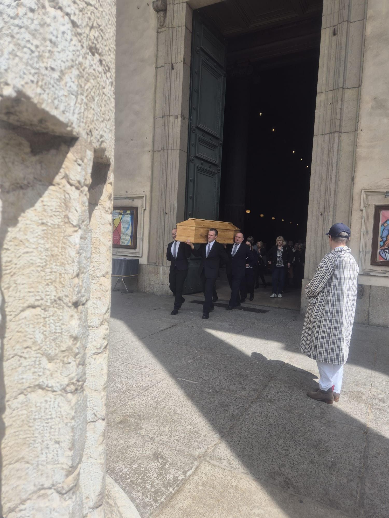 Des personnes transportent un cercueil hors d'une église. Extérieur clair.