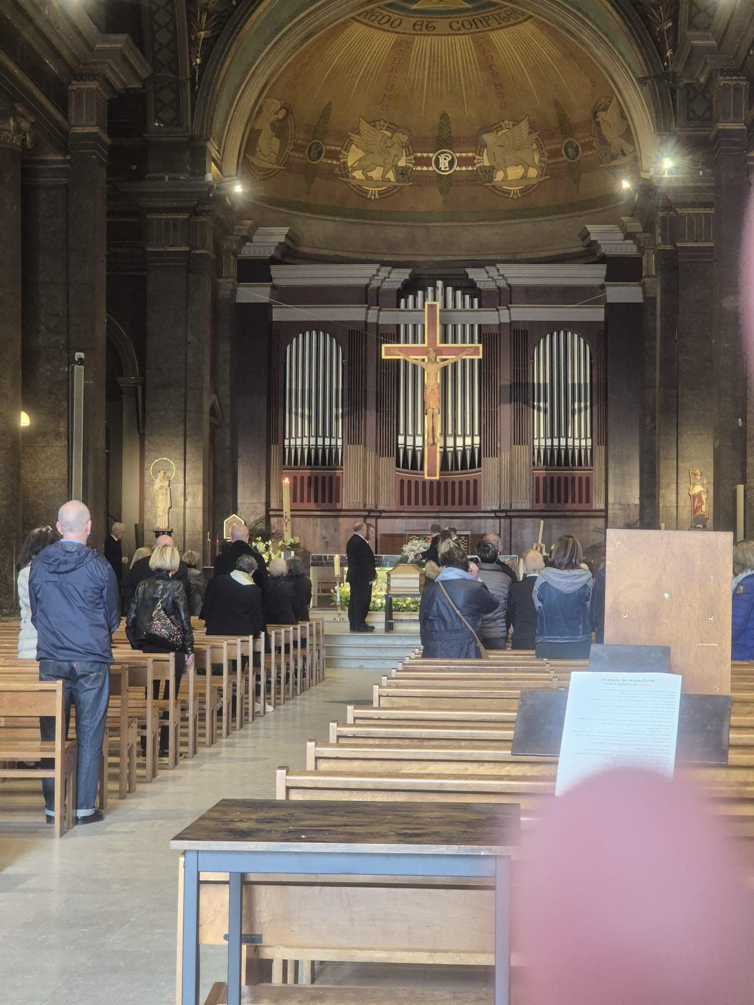 Des personnes assises dans une église, face à un autel orné d'un grand crucifix et de tuyaux d'orgue.