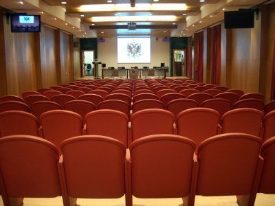 Un auditorio vacío con asientos rojos y una pantalla de proyección.
