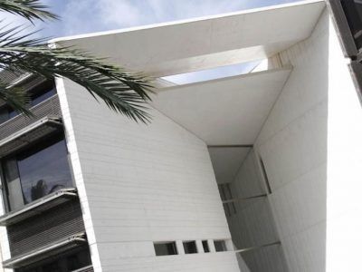 Un edificio blanco con una palmera delante.