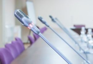 Una fila de micrófonos están colocados sobre una mesa en una sala de conferencias.