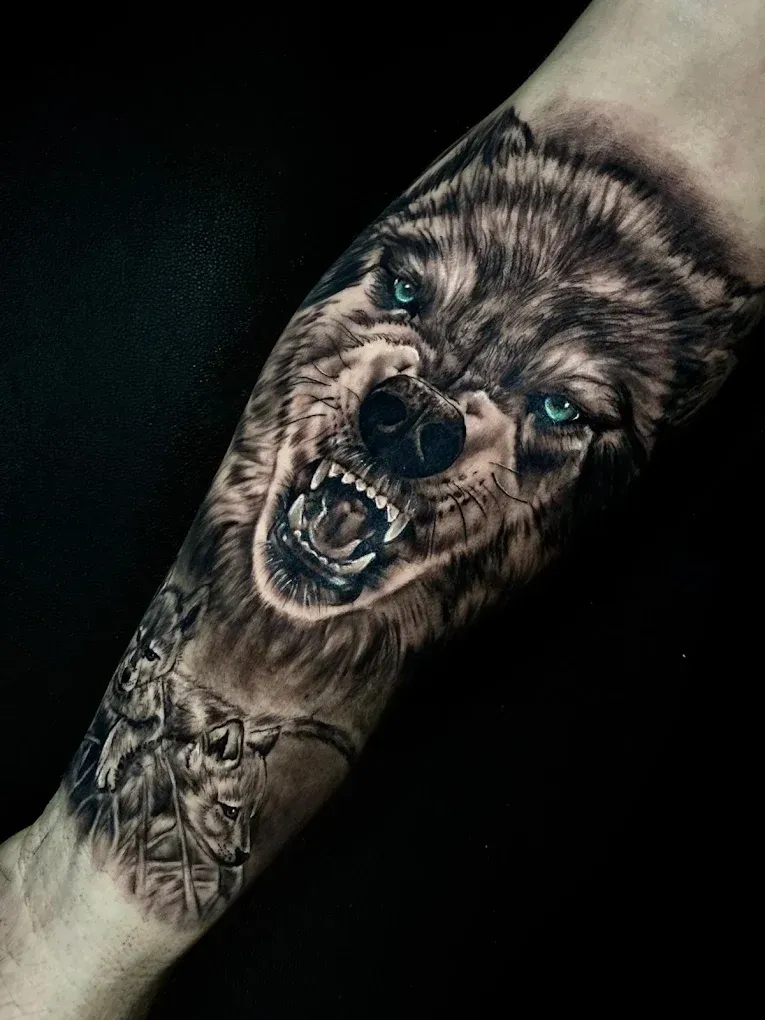 Tatuaje detallado en blanco y negro en el antebrazo que representa a un lobo gruñendo con penetrantes ojos azules.