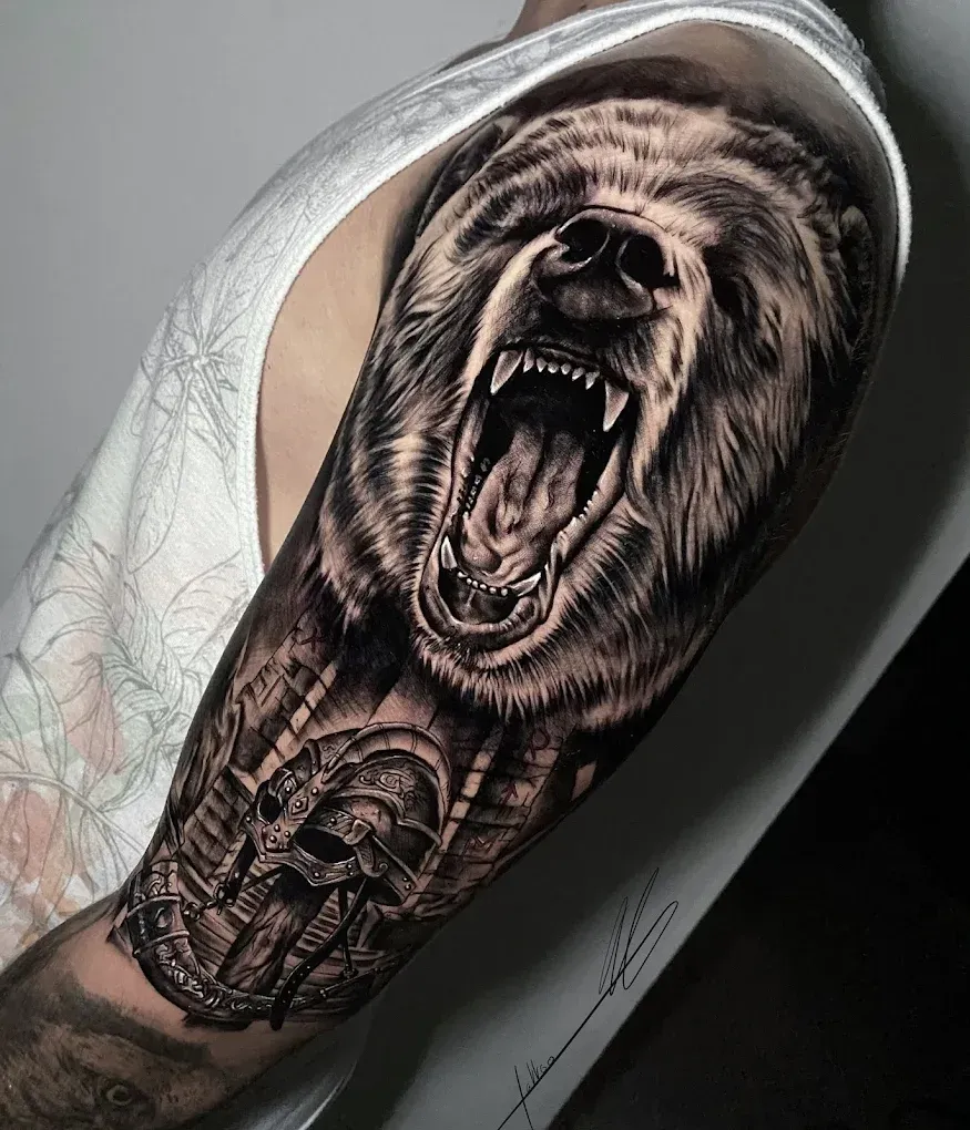 Un detallado tatuaje en blanco y negro en un brazo que muestra un oso gruñendo sobre un casco.