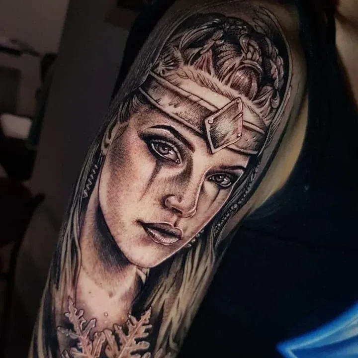 Un tatuaje detallado en blanco y negro de la figura de un guerrero que lleva una diadema metálica.