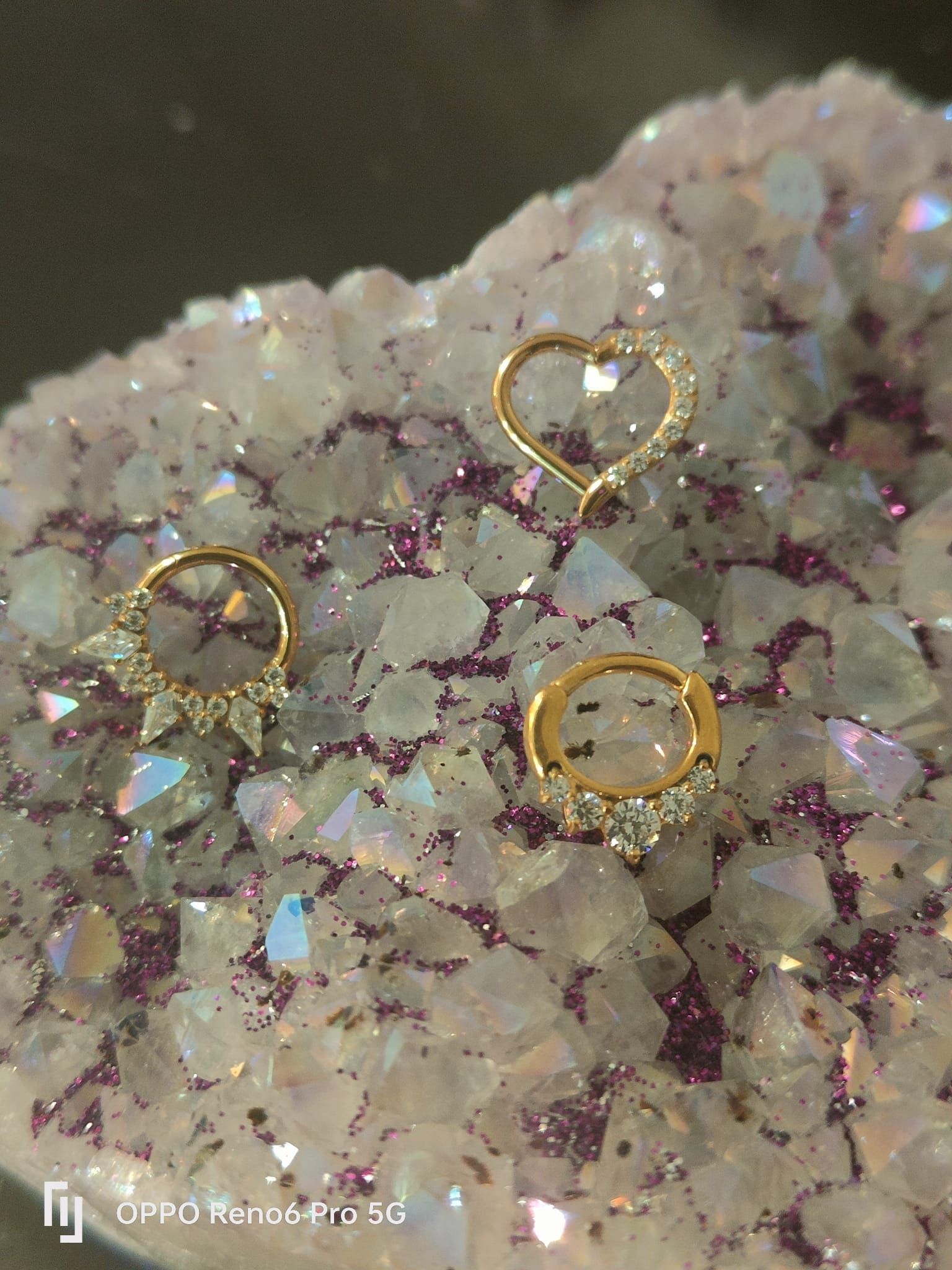 Tres pendientes de aro decorativos de oro con pequeñas piedras incrustadas, dispuestos sobre una superficie de cristal.