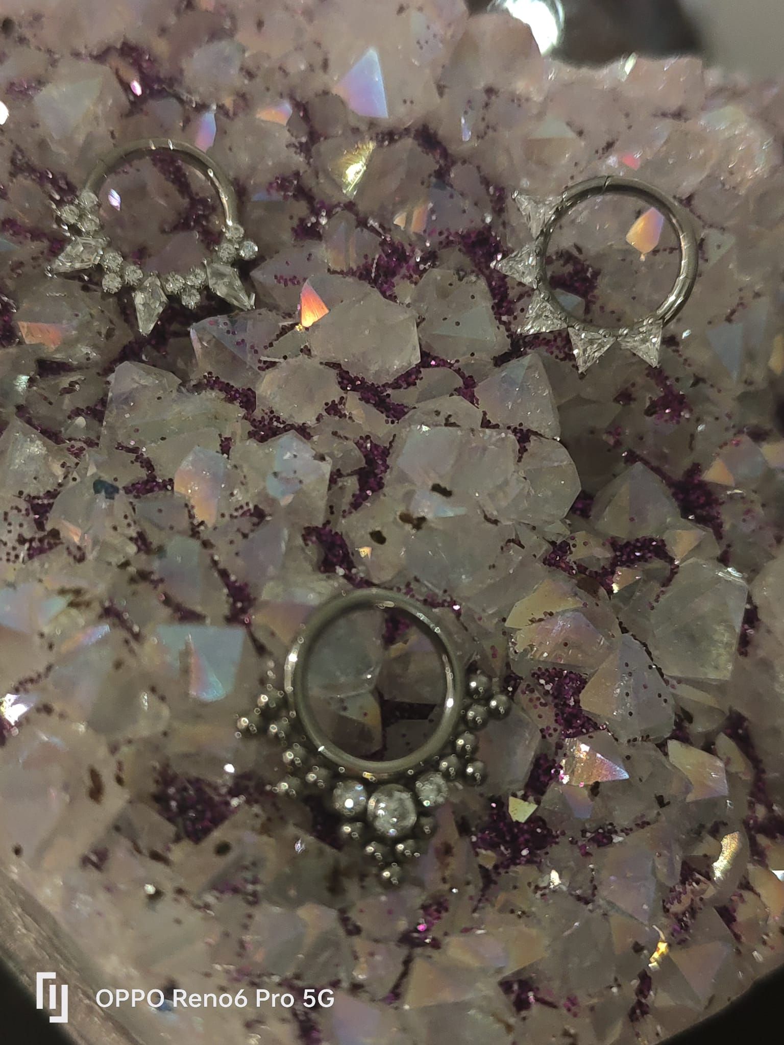 Tres aros decorativos de metal para el tabique nasal, apoyados sobre un trozo de cristal de amatista en bruto.