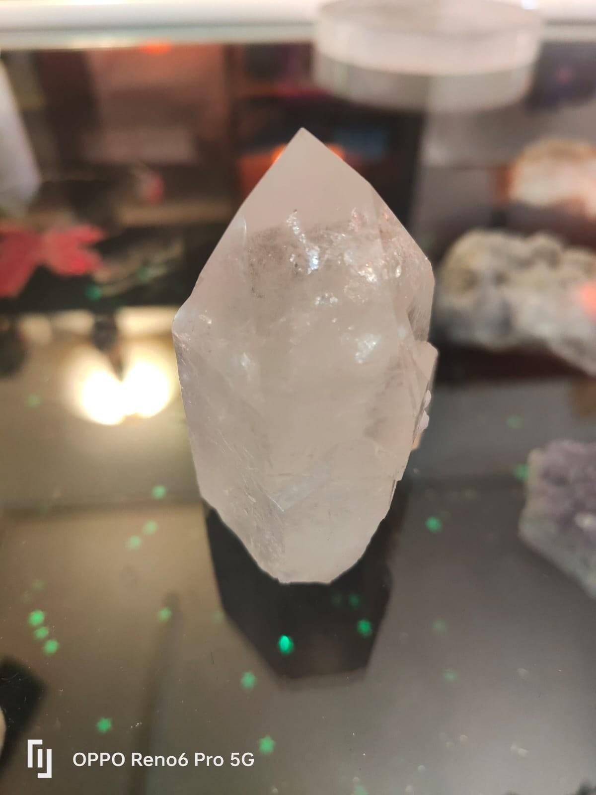 Una punta de cristal de cuarzo transparente de seis caras reposa sobre una superficie reflectante.