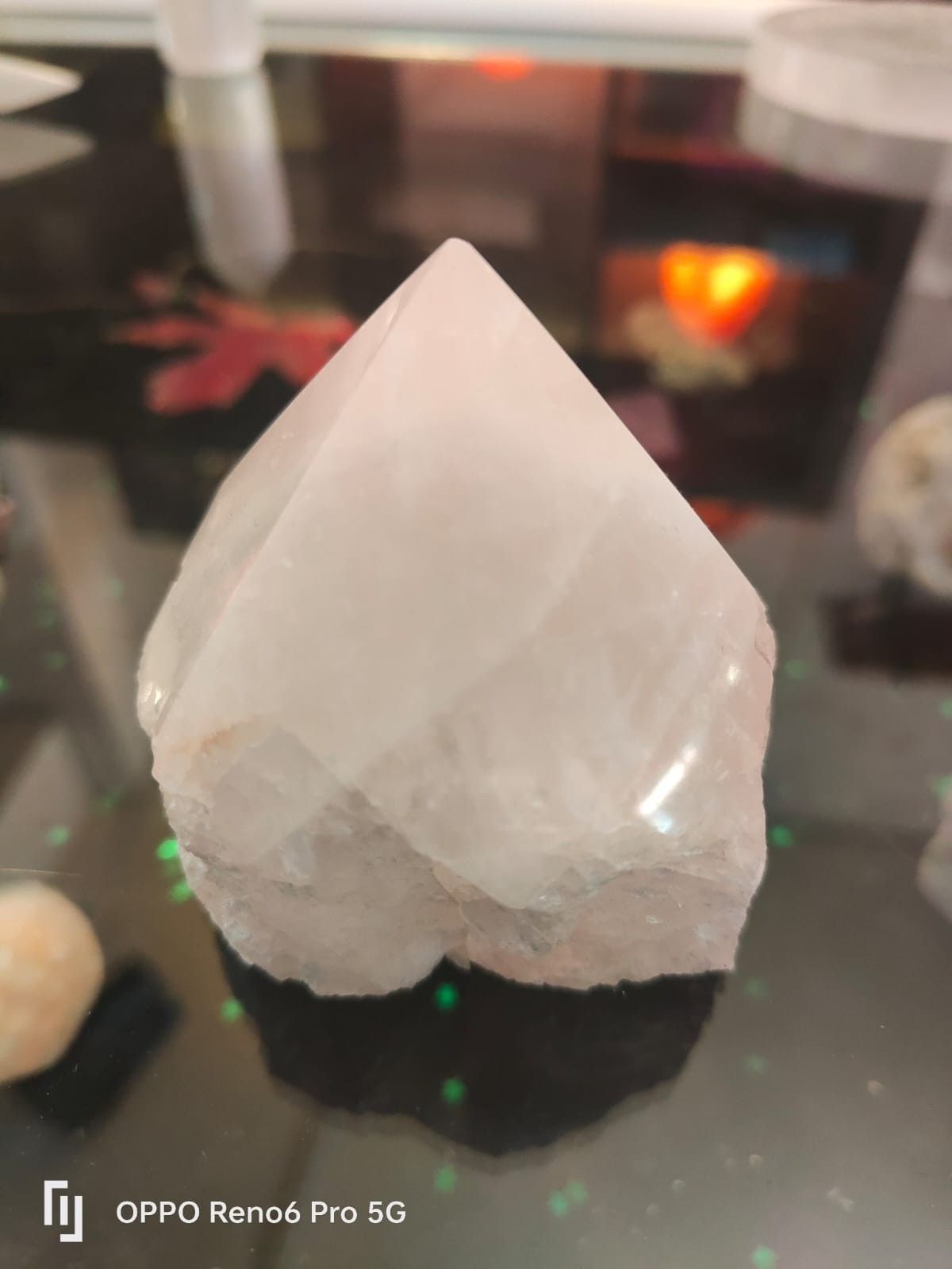 Una punta de cristal translúcida de color claro reposa sobre una superficie negra reflectante.