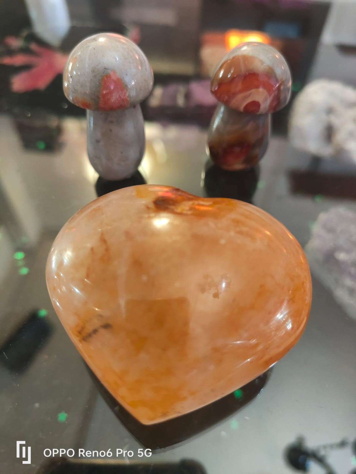 Dos pequeñas setas de piedra tallada se alzan detrás de un corazón de cristal naranja pulido.