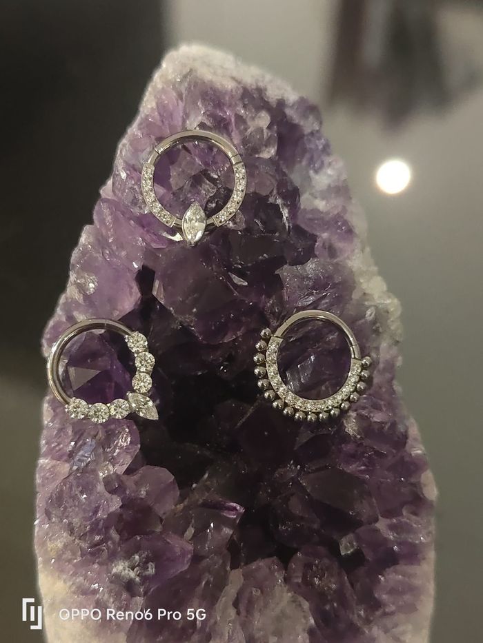 Una colección de varios pendientes de aro y piercings nasales de metal plateado, algunos con piedras preciosas.