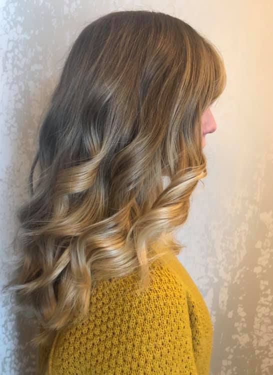 Frau mit gewelltem blonden und hellbraunen Haar, die einen gelben Pullover trägt.