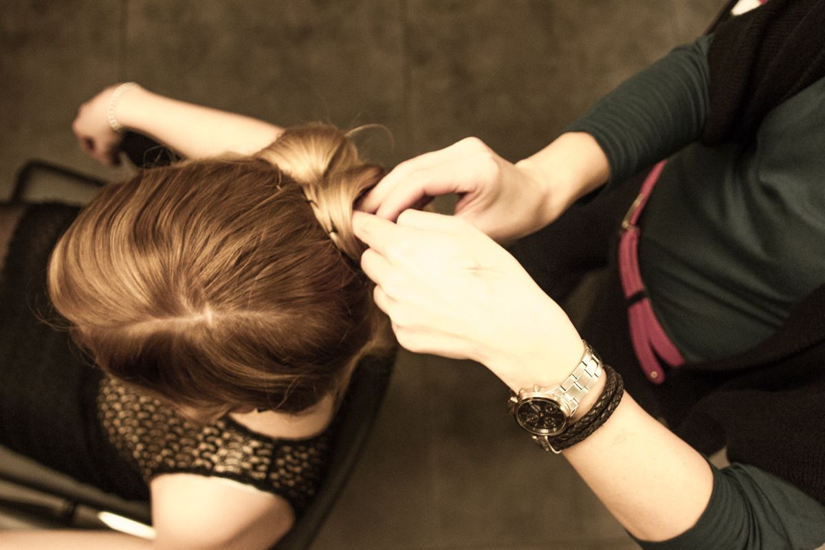 Eine Person lässt sich von einer anderen Person die Haare stylen; in einem Innenraum.