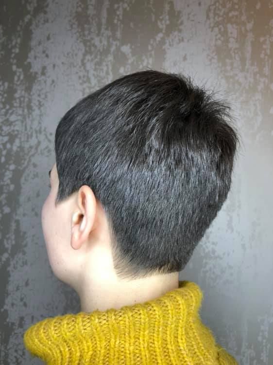 Frau mit kurzem, dunklem Haar, das im Nacken und an den Seiten kurz geschnitten ist, trägt einen gelben Pullover.