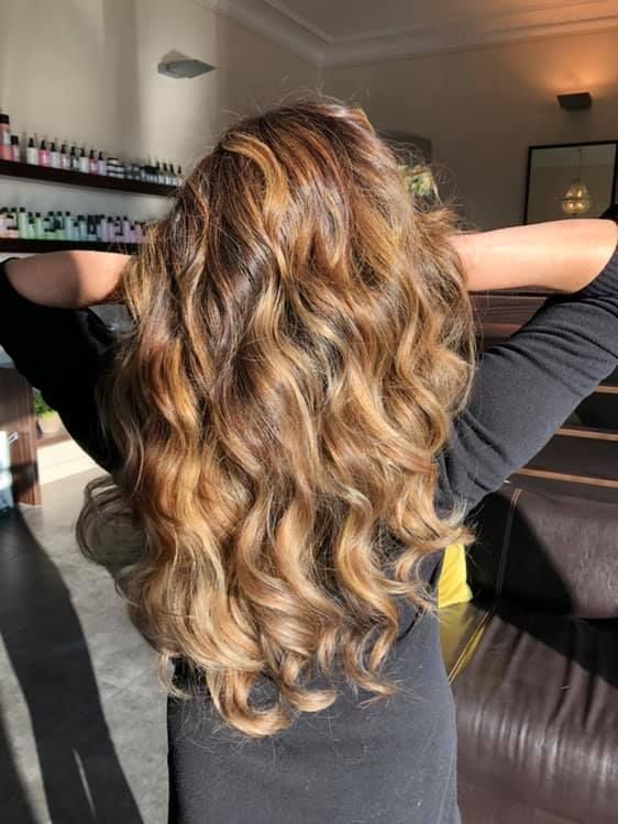 Frau mit gewelltem, hellbraunem Haar, die Arme hinter dem Kopf erhoben, sonnige Innenaufnahme.