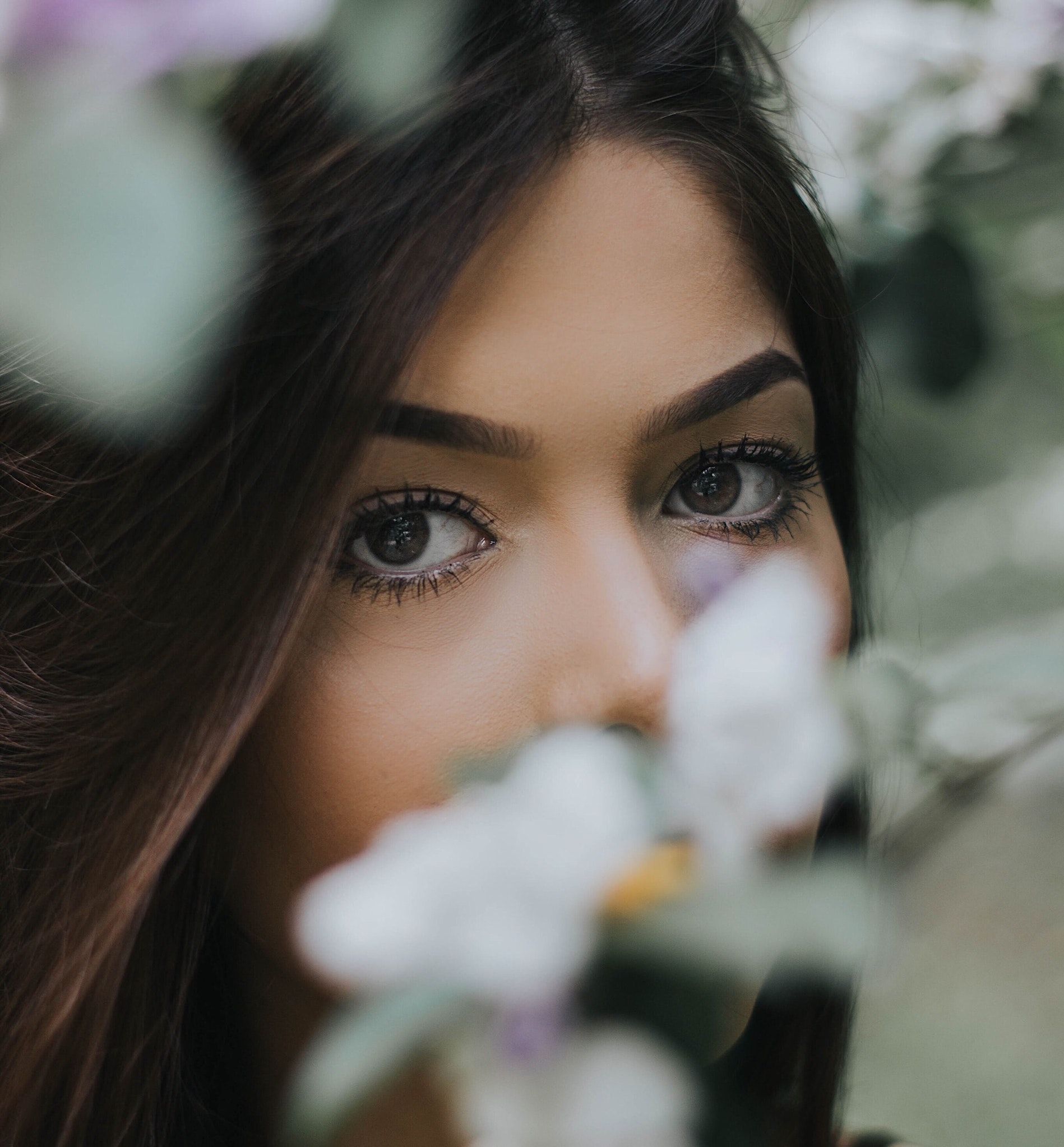 Nahaufnahme von den Augen und dem Gesicht einer Person, umrahmt von weichgezeichneten weißen und violetten Blumen.