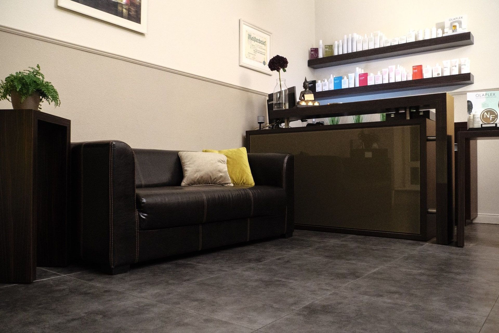 Ein Wartebereich mit schwarzer Ledercouch, Holztheke und Regalen mit Produkten.