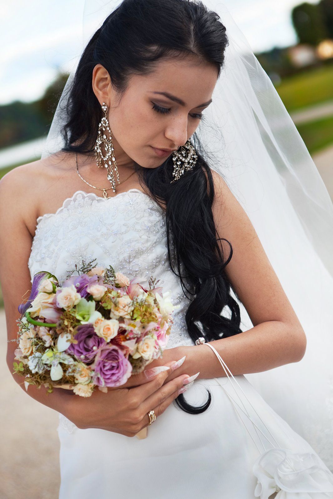 Braut im weißen Kleid, die Brautstrauß, Schleier und lange Ohrringe hält. Blick nach unten.