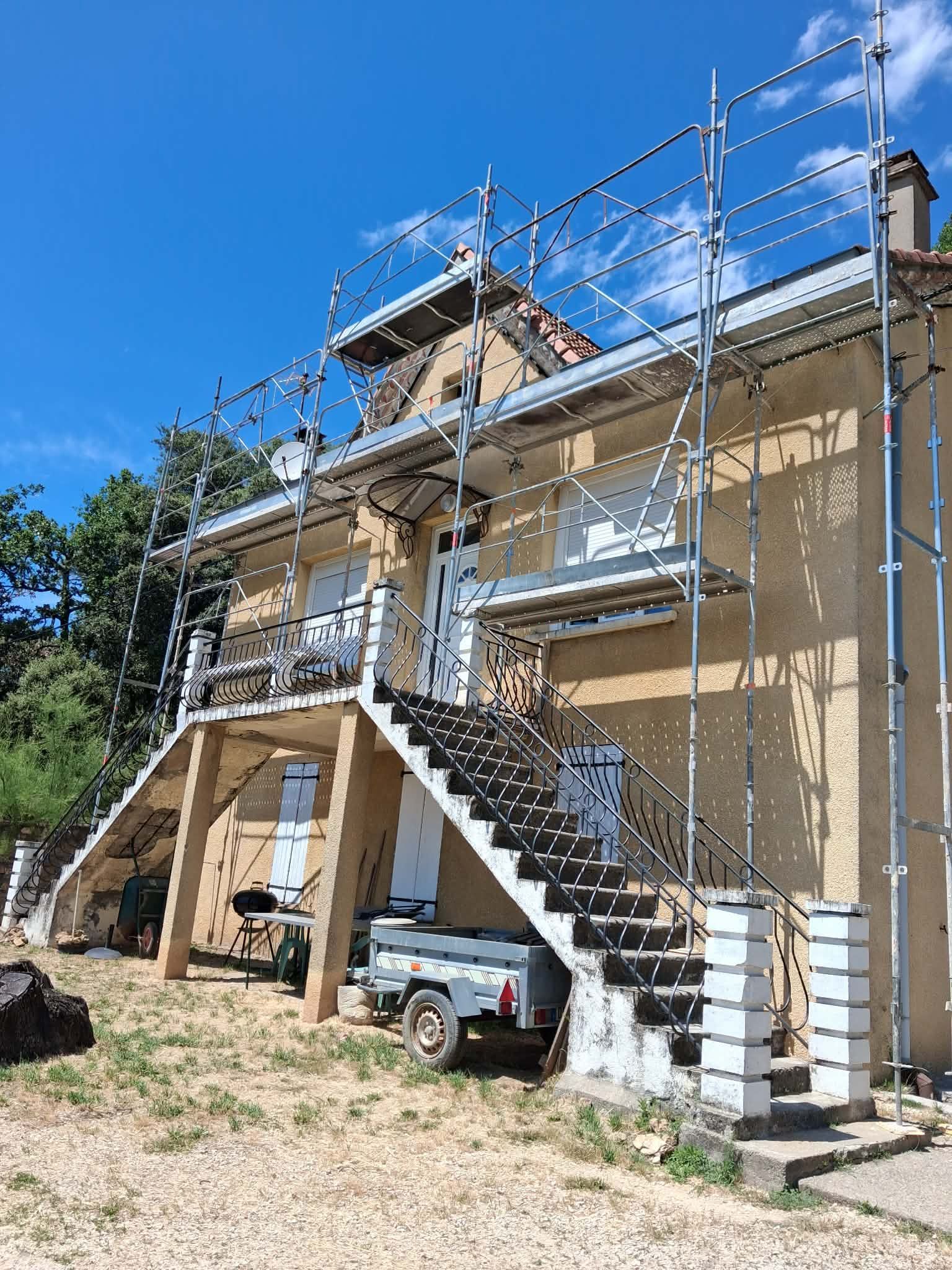 Une maison avec une grosse toiture entourée d'échafaudages et de filets de protection