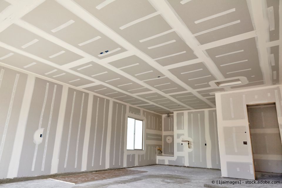 Innenansicht eines im Bau befindlichen Raumes, dessen Wände und Decke bereits mit Gipskartonplatten verkleidet sind.