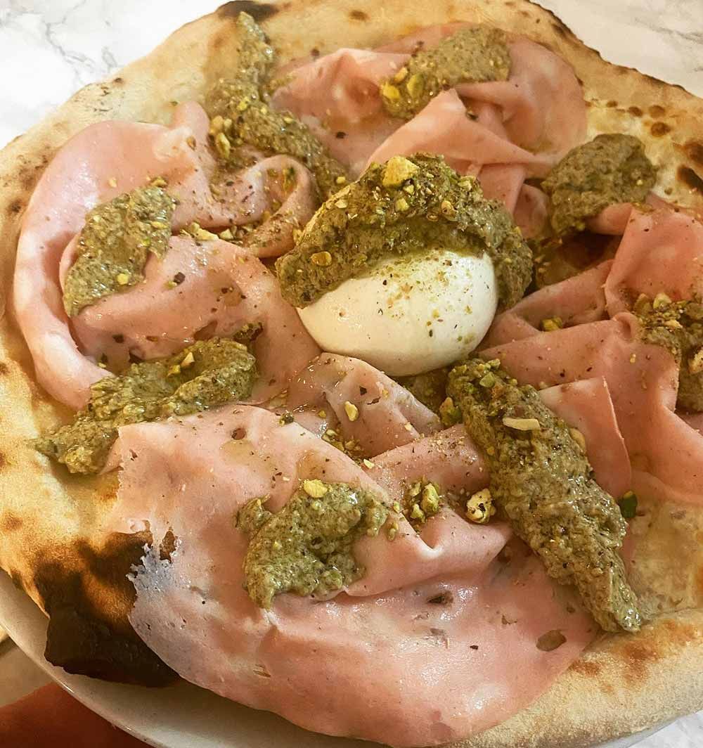 Pizza cubierta con mortadela, pesto y huevo blando.