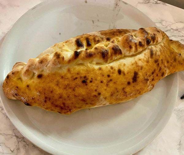 Un calzone de color marrón dorado en un plato blanco, con manchas carbonizadas en la corteza.