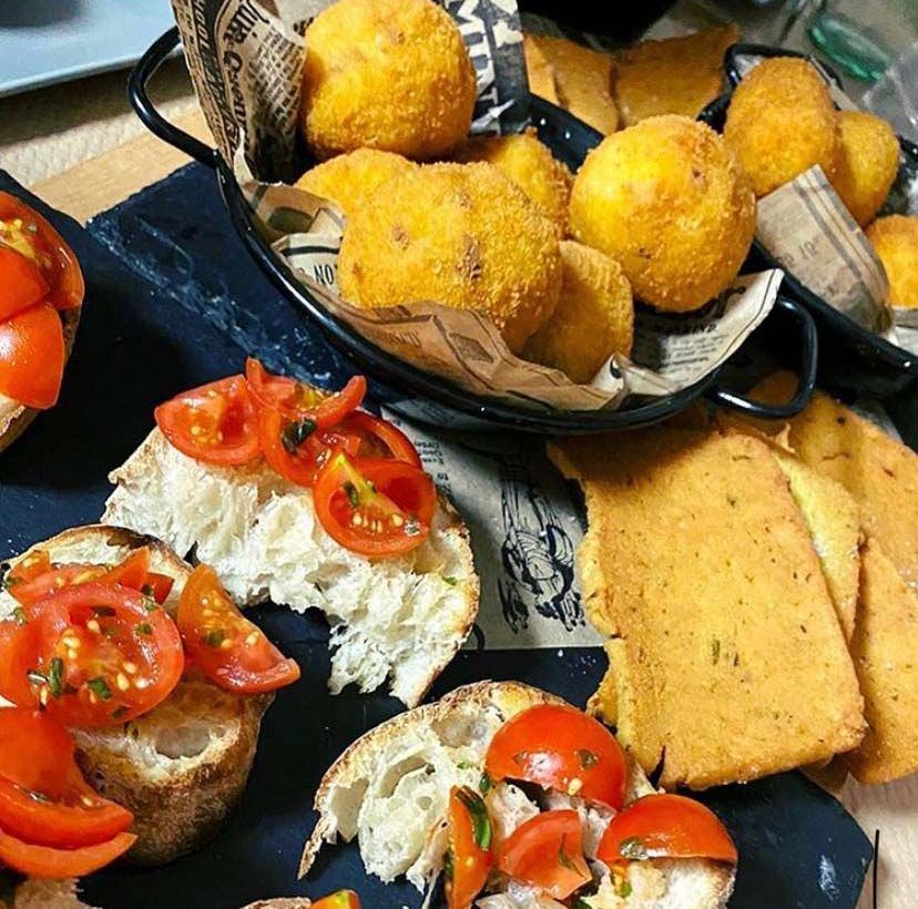 Bruschetta cubierta con tomates, arancini fritos y polenta en una bandeja de pizarra.