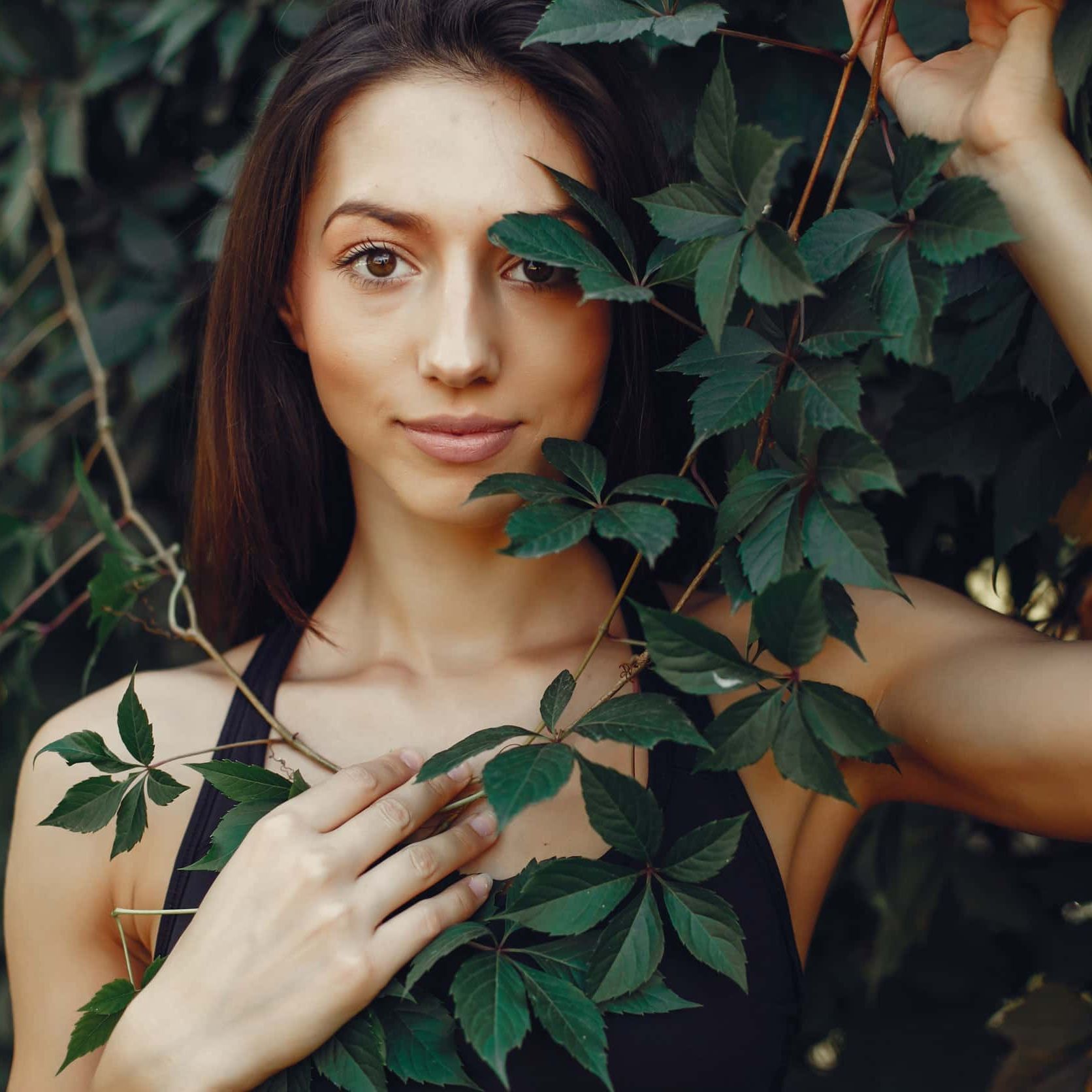 Una mujer con un top negro está rodeada de hojas verdes.
