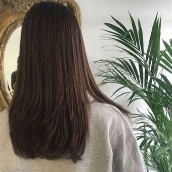 Una mujer con cabello largo y castaño está parada frente a un espejo y una palmera.