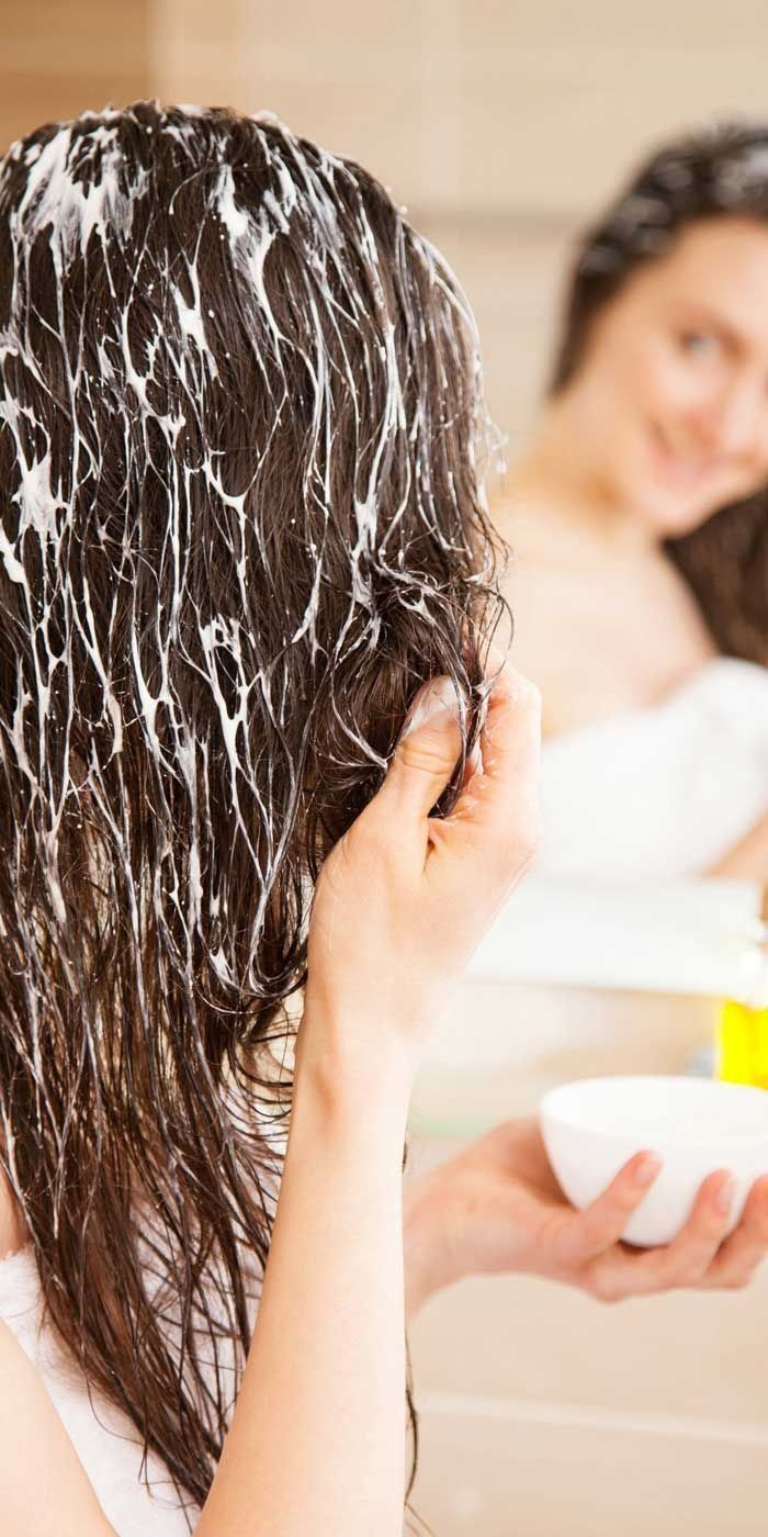 Una mujer se aplica un acondicionador en el cabello frente a un espejo.