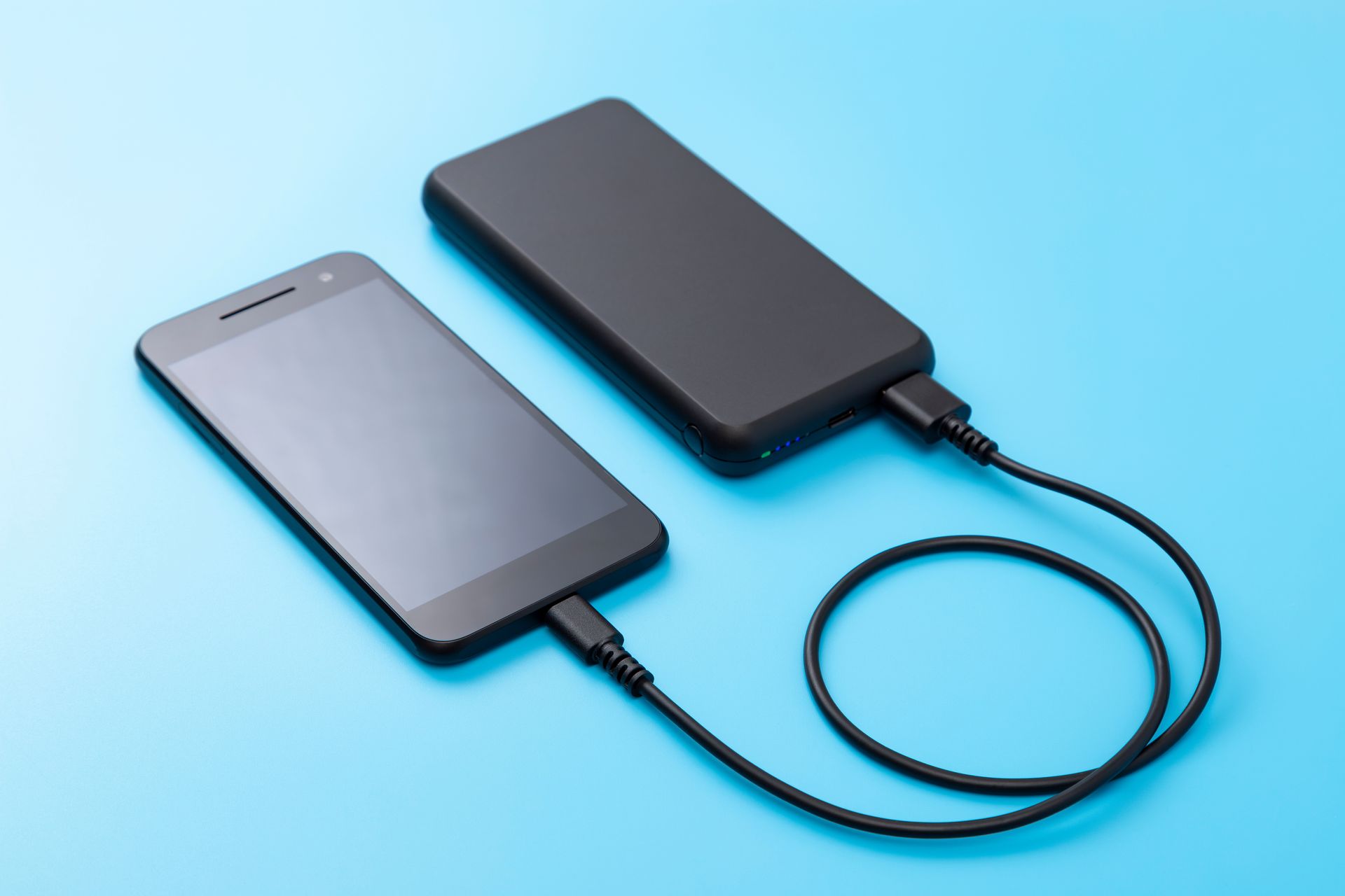 Un téléphone posé sur un fond bleu relié à son chargeur