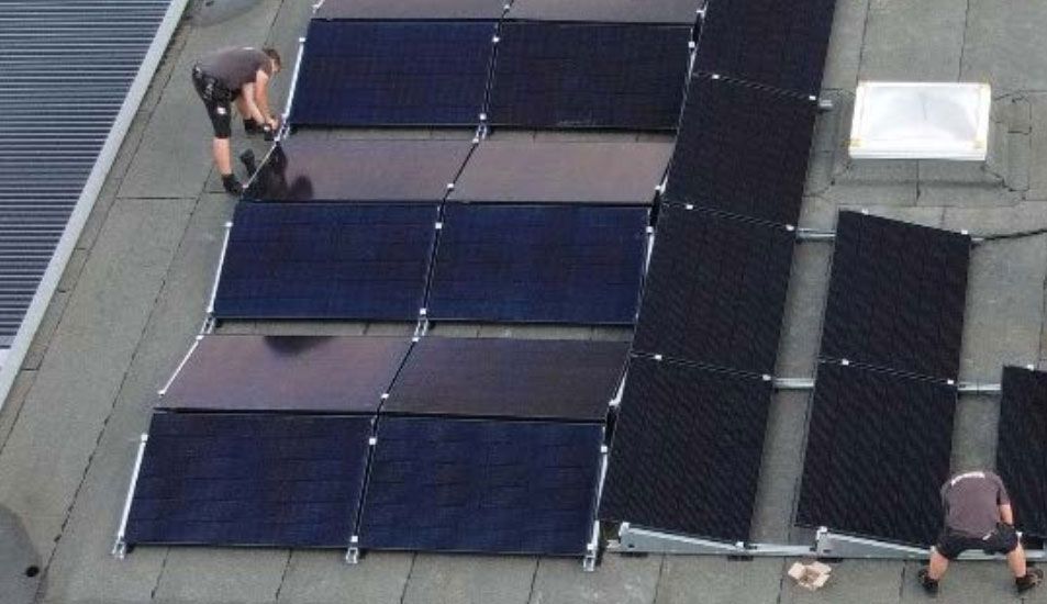 Zwei Männer arbeiten an Solarmodulen auf dem Dach eines Gebäudes