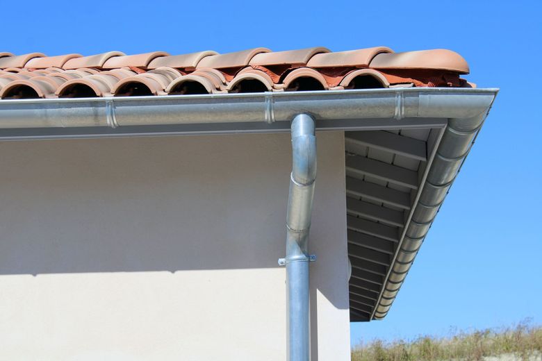 Coin de toit de maison avec des tuiles en terre cuite et une gouttière argentée.