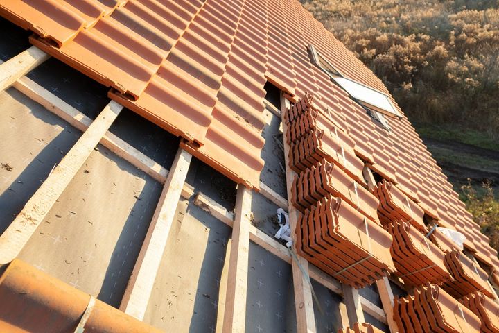 Toiture en construction avec tuiles rouges et charpente en bois apparente.