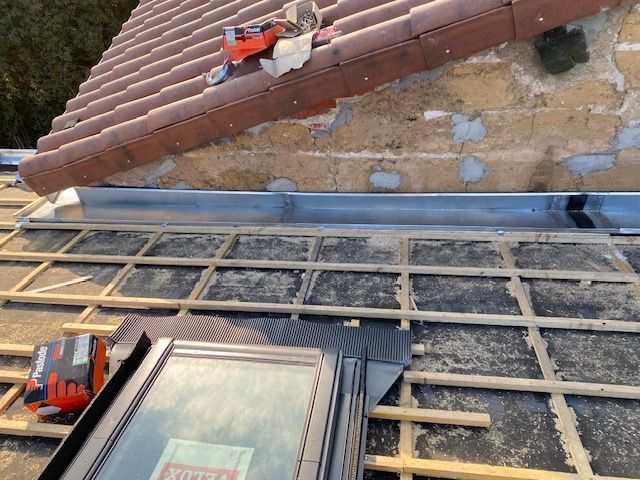 Travaux de toiture sur un toit de tuiles avec échafaudages et matériaux à côté d'un mur en pierre.