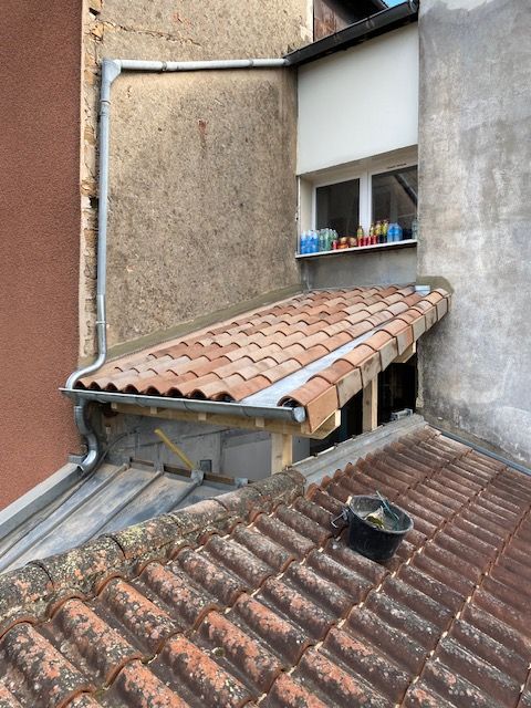 Vue depuis le toit avec une toiture en tuiles rouges, une petite lucarne et des murs en stuc patinés.