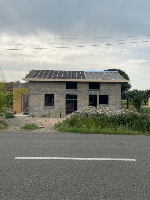 Petite maison en béton inachevée avec panneaux solaires, en bord de route.