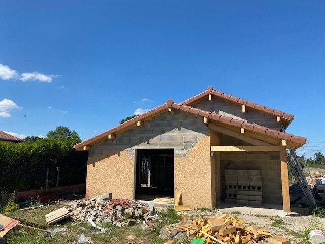 Maison partiellement construite avec toit apparent, murs inachevés et débris de construction devant.