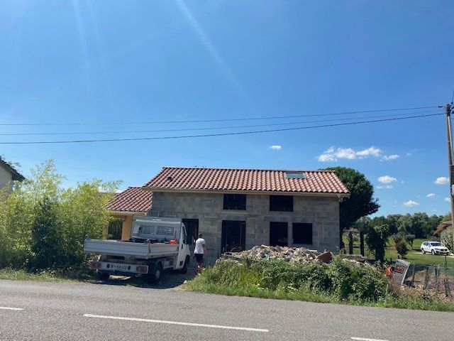 Maison en construction avec toit de tuiles rouges, une camionnette garée devant.
