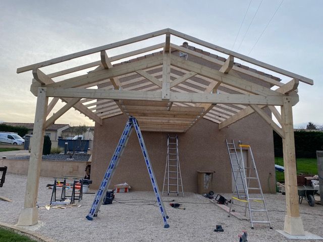 Un abri de voiture en cours de construction, avec des échelles et des outils à l'extérieur.