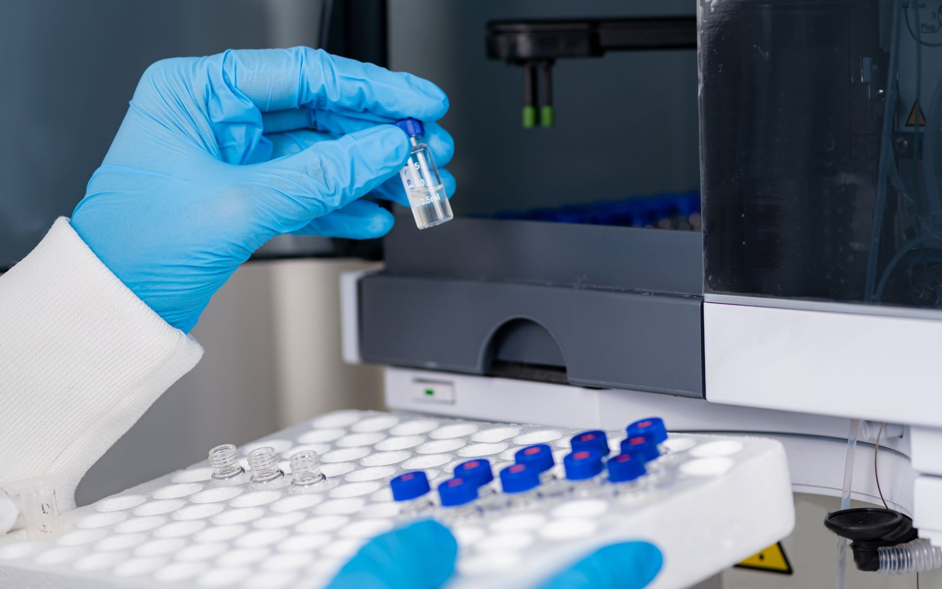 Una persona que lleva guantes azules sostiene una pequeña botella en un laboratorio.