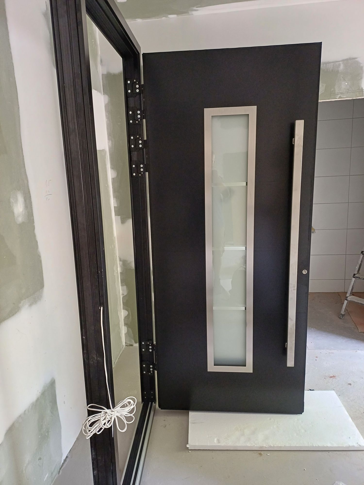 In einem Raum steht eine schwarze Tür mit einem Edelstahlgriff.