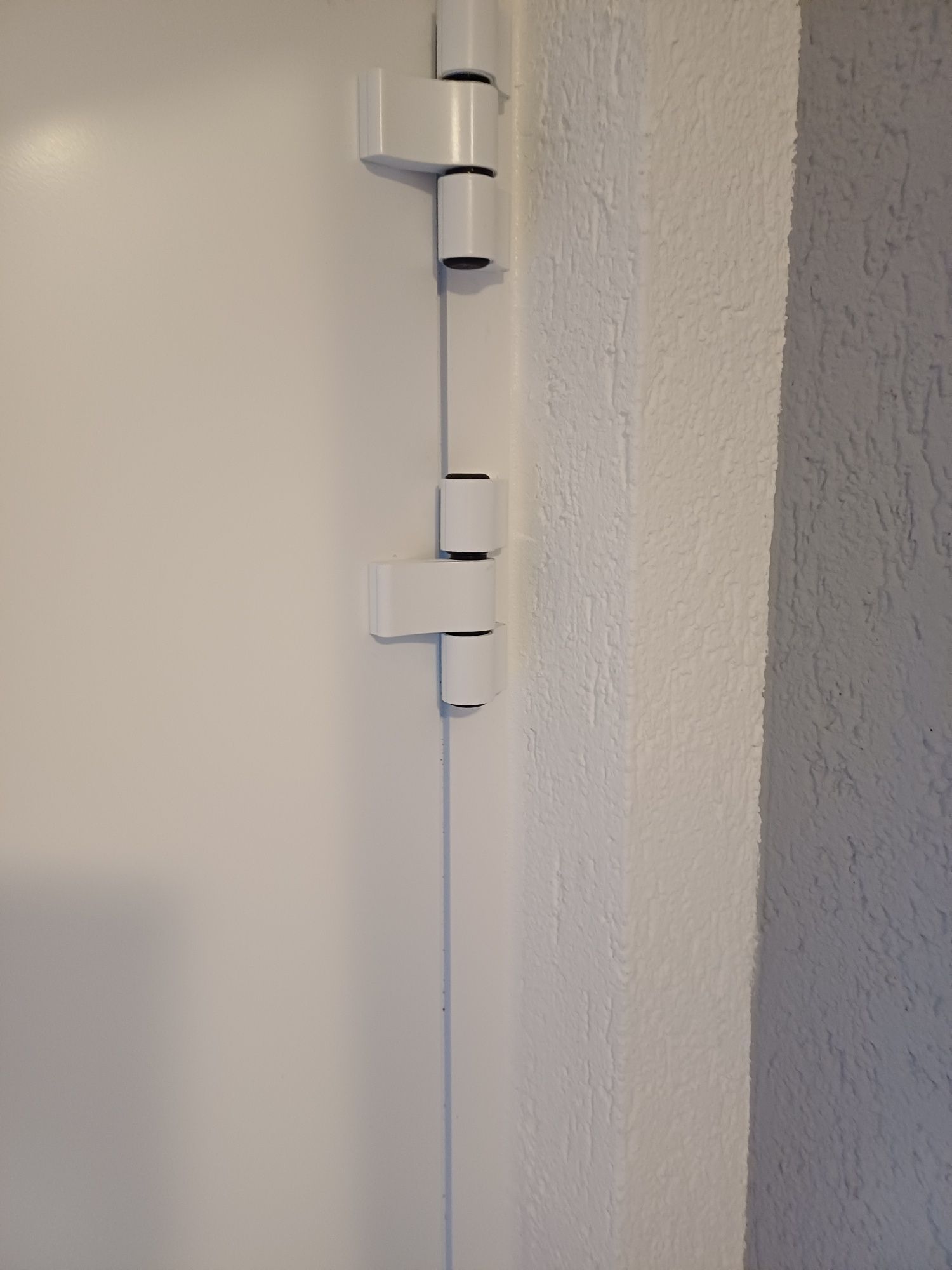 Eine Nahaufnahme eines weißen Türscharniers an einer weißen Wand.