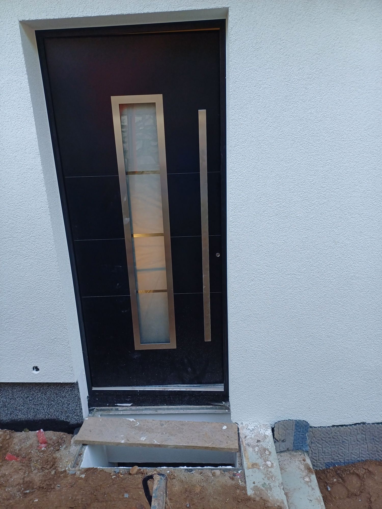 An einer weißen Wand steht eine schwarze Tür mit einem Edelstahlgriff.